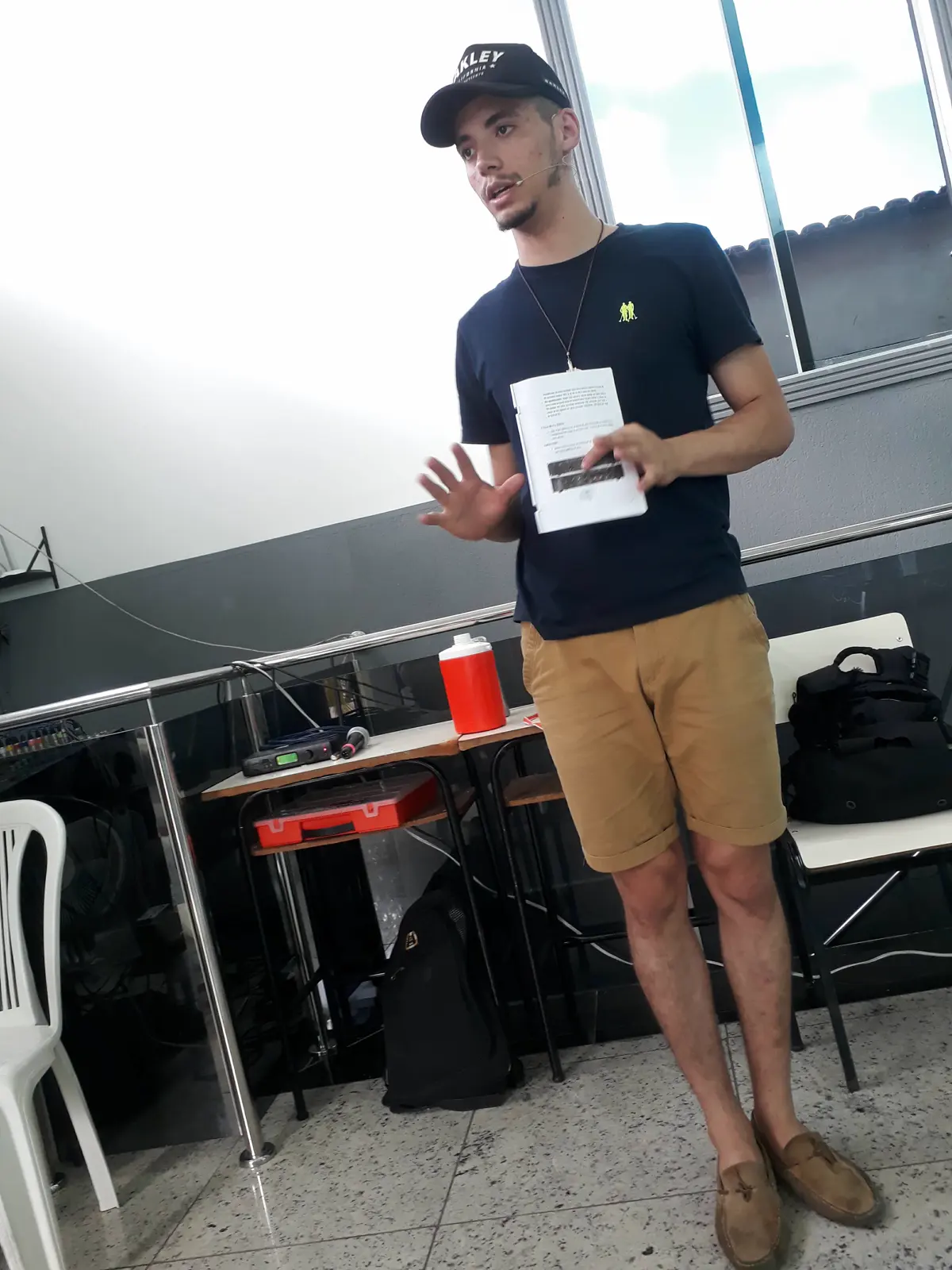 Matheus Borges dando aula presencial de áudio, de pé, segurando o material da aula.
