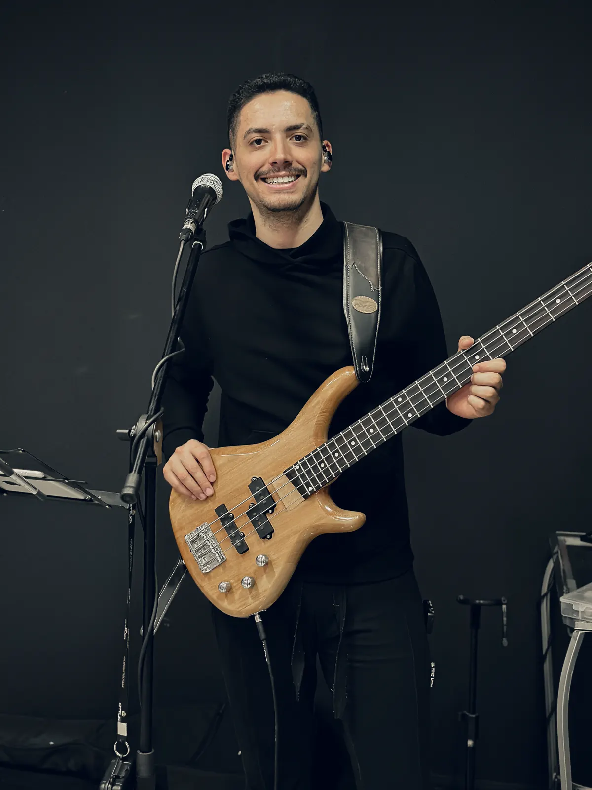 Matheus Borges sorrindo no palco, com fone de retorno no ouvido e um baixo.